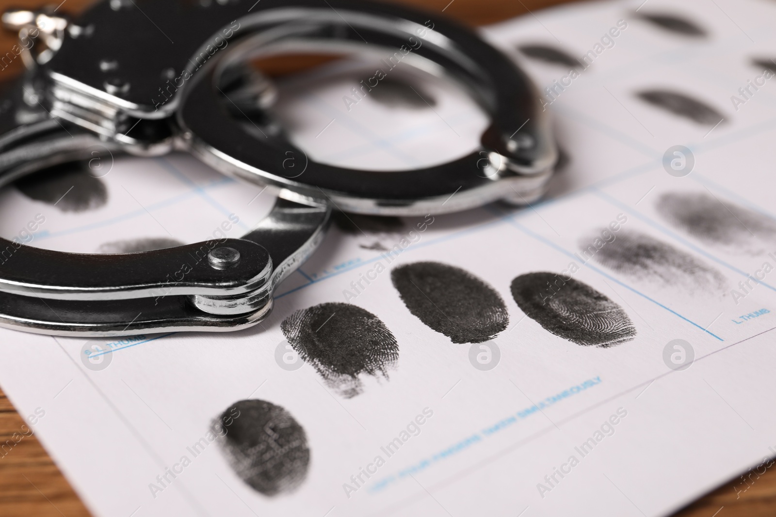 Photo of Paper sheet with human fingerprints and handcuffs on table, closeup. Criminal conviction