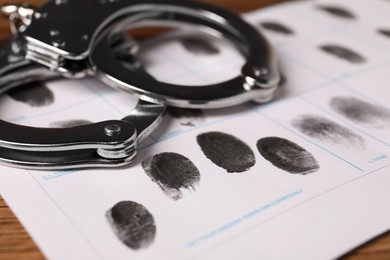 Photo of Paper sheet with human fingerprints and handcuffs on table, closeup. Criminal conviction