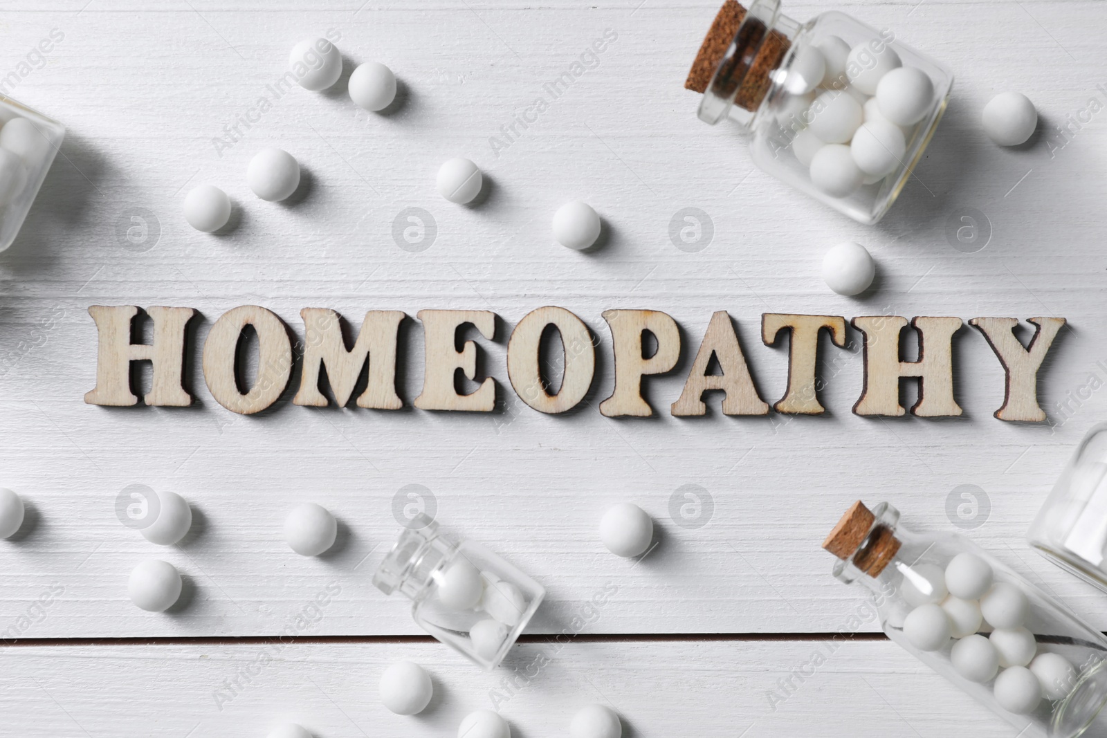 Photo of Word Homeopathy and pills on white wooden background, flat lay