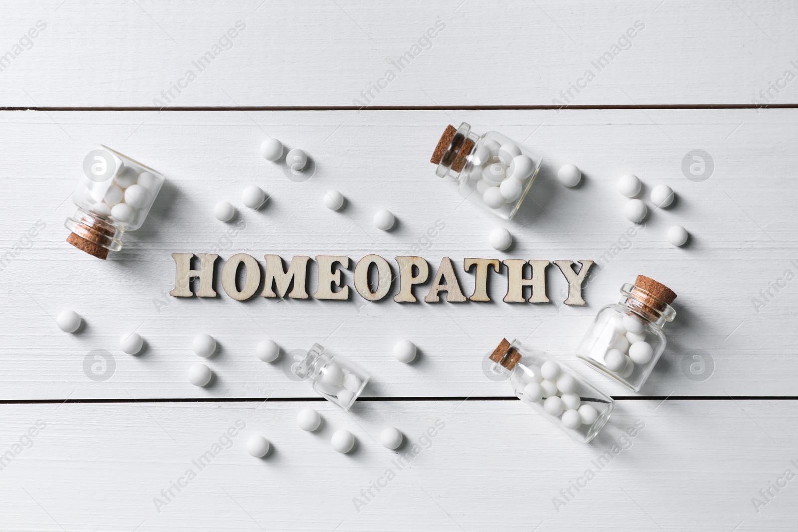 Photo of Word Homeopathy and pills on white wooden background, flat lay