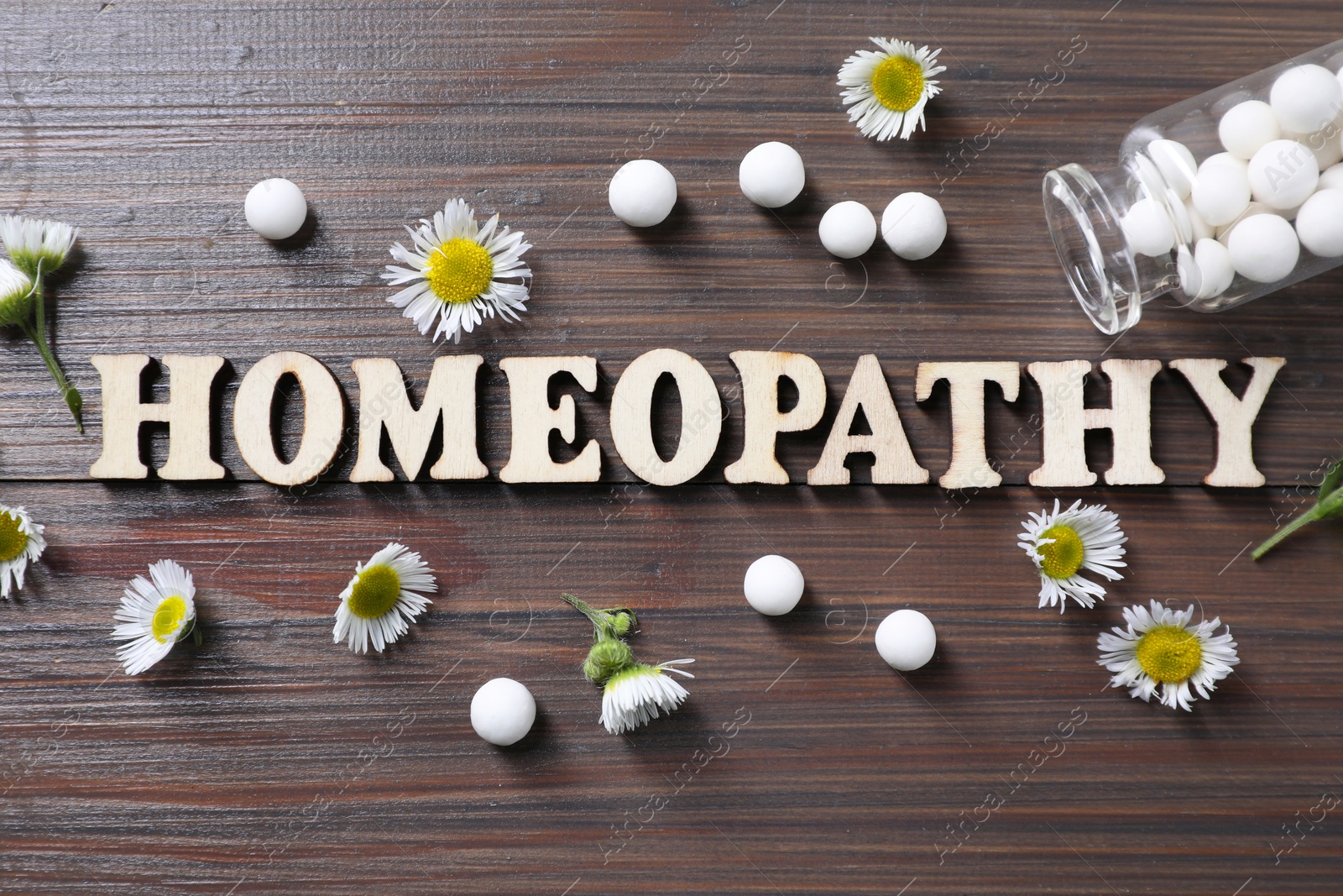 Photo of Word Homeopathy, chamomile flowers and pills on wooden background, flat lay