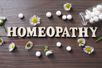 Word Homeopathy, chamomile flowers and pills on wooden background, flat lay