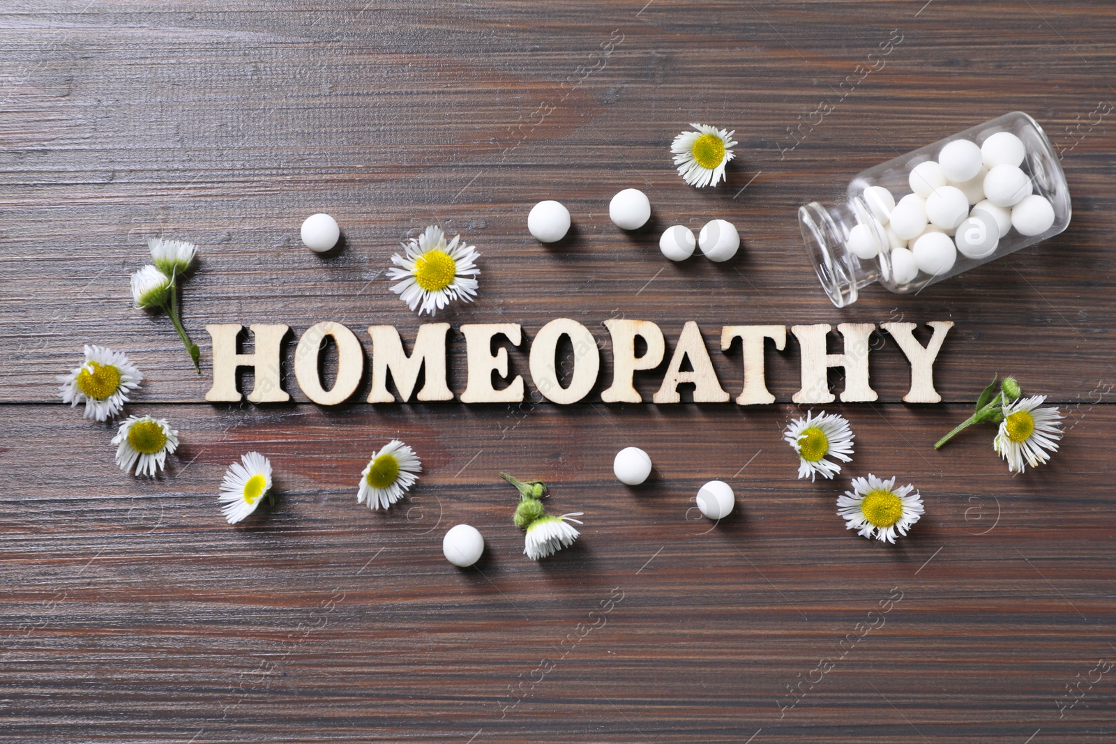 Photo of Word Homeopathy, chamomile flowers and pills on wooden background, flat lay