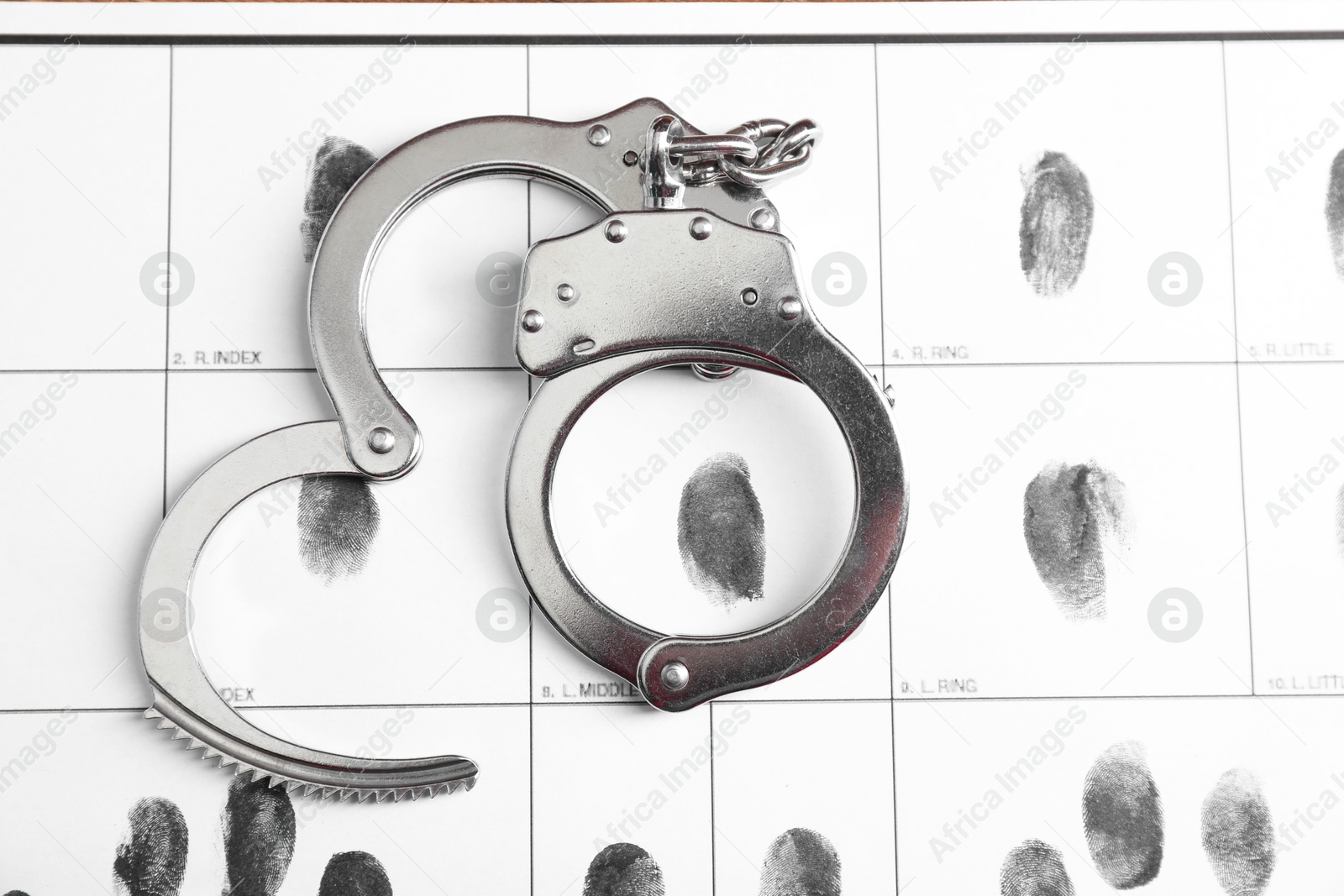 Photo of Human fingerprints and handcuffs on paper, top view. Criminal conviction