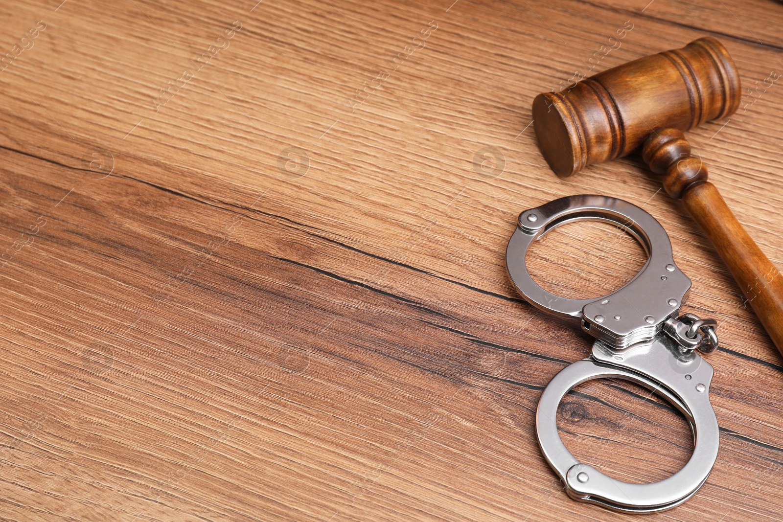 Photo of Judge's gavel and handcuffs on wooden table. Space for text