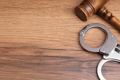 Photo of Judge's gavel and handcuffs on wooden table, above view. Space for text