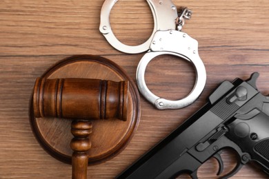 Judge's gavel, handcuffs and gun on wooden table, flat lay