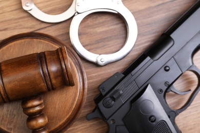 Photo of Judge's gavel, handcuffs and gun on wooden table, flat lay