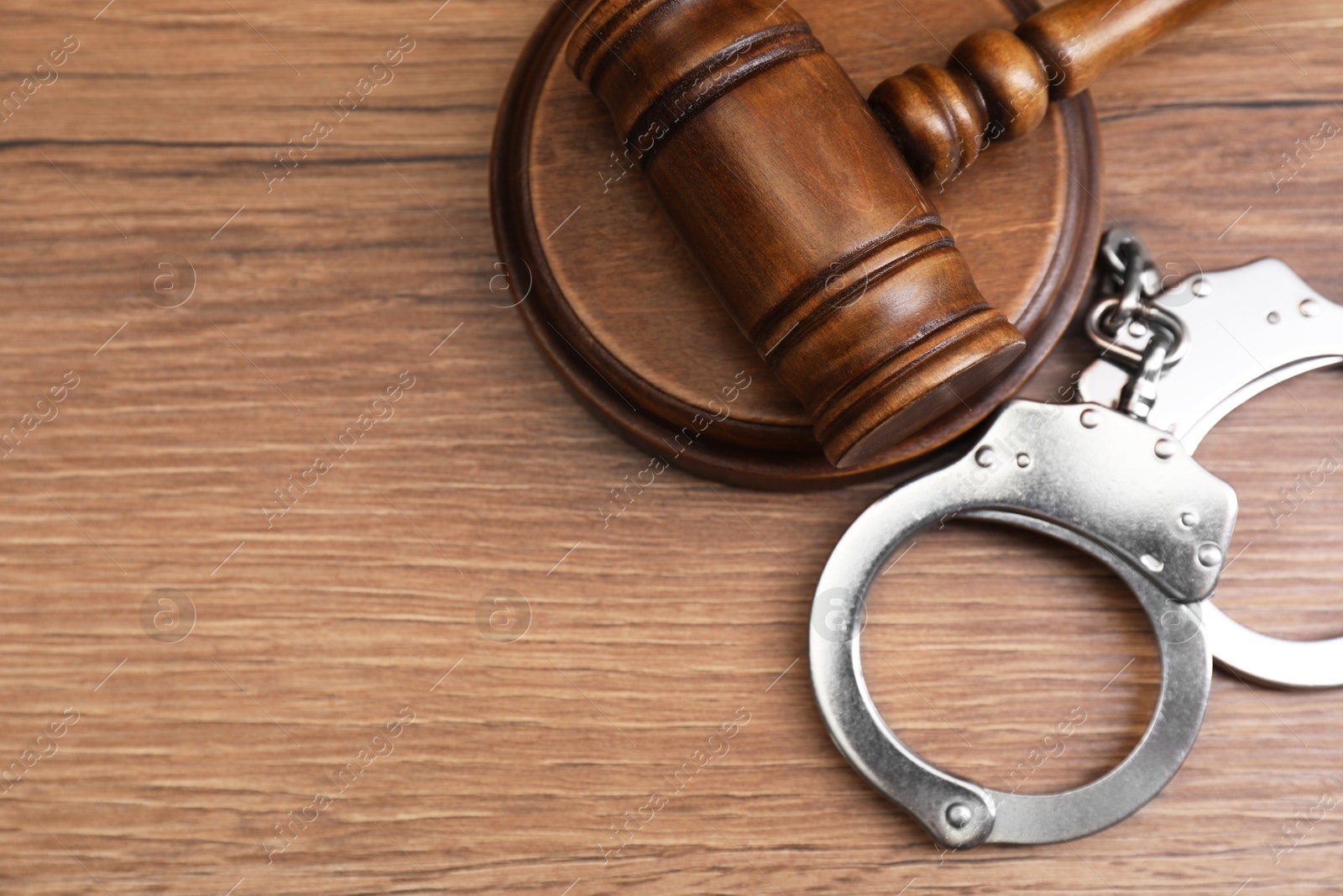 Photo of Judge's gavel and handcuffs on wooden table, flat lay. Space for text