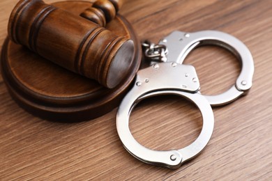 Photo of Judge's gavel and handcuffs on wooden table, closeup