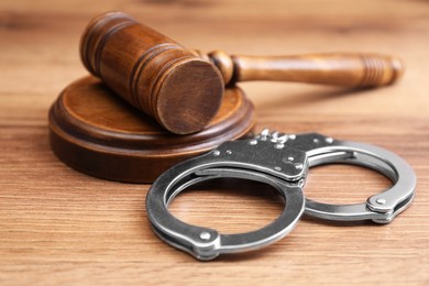 Photo of Judge's gavel and handcuffs on wooden table, closeup