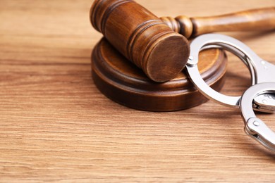 Photo of Judge's gavel and handcuffs on wooden table, closeup. Space for text