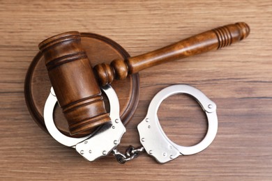 Photo of Judge's gavel and handcuffs on wooden table, top view