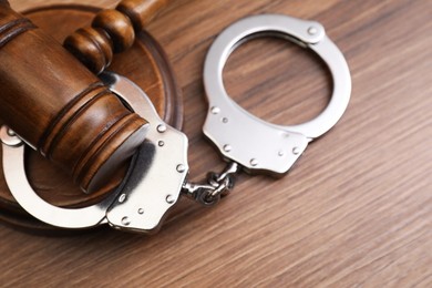 Judge's gavel and handcuffs on wooden table, top view