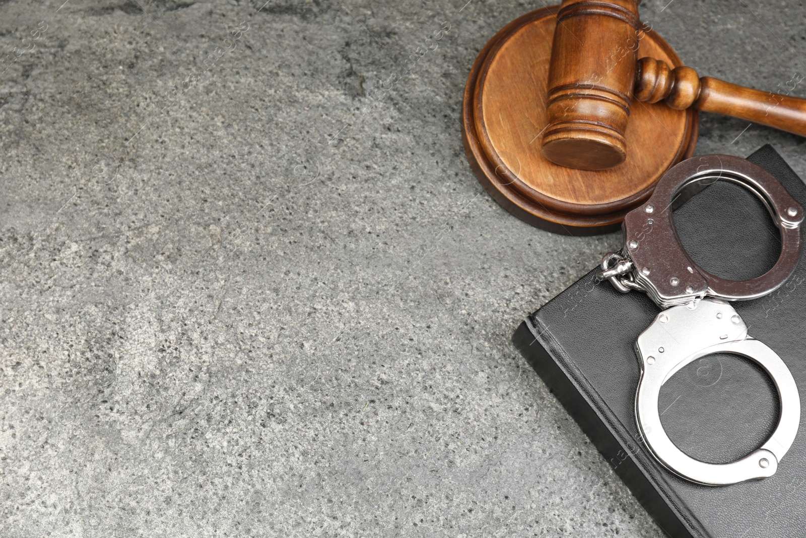 Photo of Book, judge's gavel and handcuffs on gray textured table, above view. Space for text