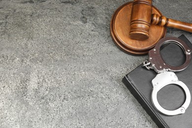 Book, judge's gavel and handcuffs on gray textured table, above view. Space for text