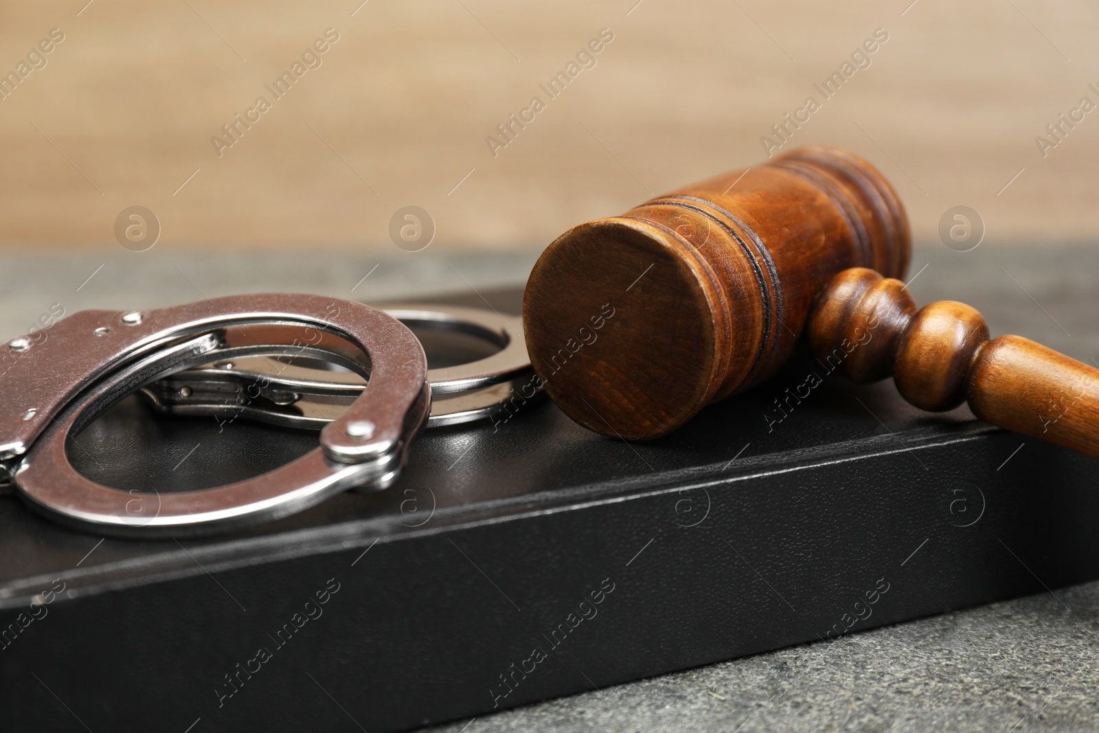 Photo of Book, judge's gavel and handcuffs on gray textured table, closeup