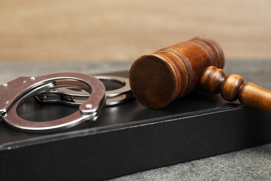 Book, judge's gavel and handcuffs on gray textured table, closeup