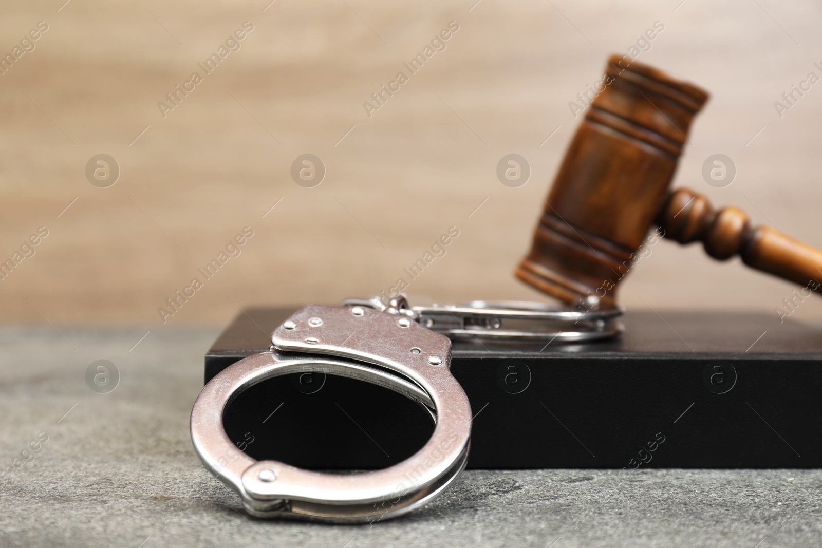 Photo of Book, judge's gavel and handcuffs on gray textured table, closeup. Space for text