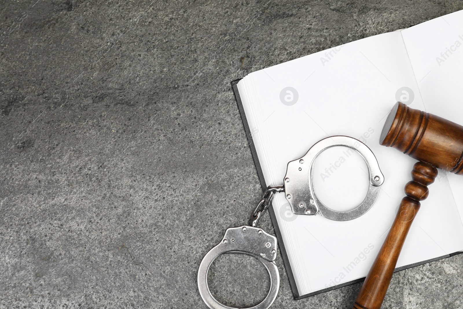 Photo of Book, judge's gavel and handcuffs on gray textured table, flat lay. Space for text