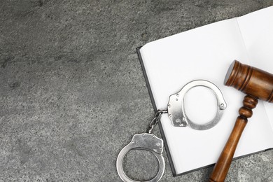 Book, judge's gavel and handcuffs on gray textured table, flat lay. Space for text