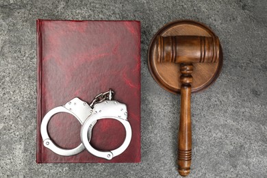 Book, judge's gavel and handcuffs on gray textured table, flat lay