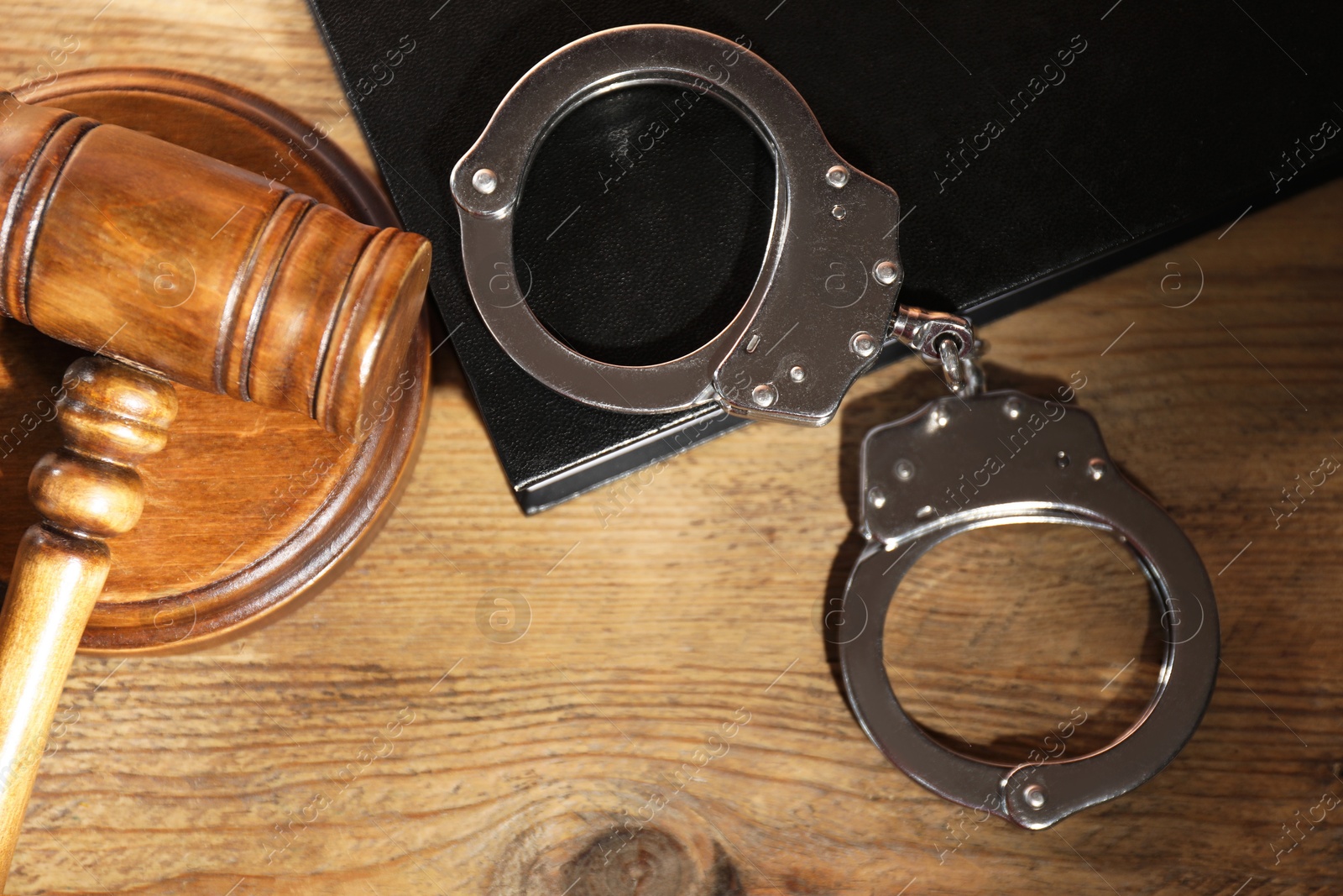 Photo of Book, judge's gavel and handcuffs on wooden table, flat lay