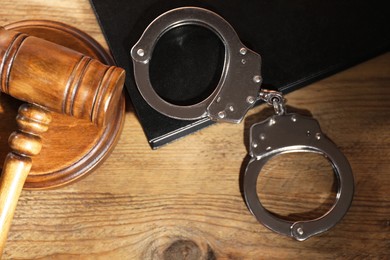 Book, judge's gavel and handcuffs on wooden table, flat lay