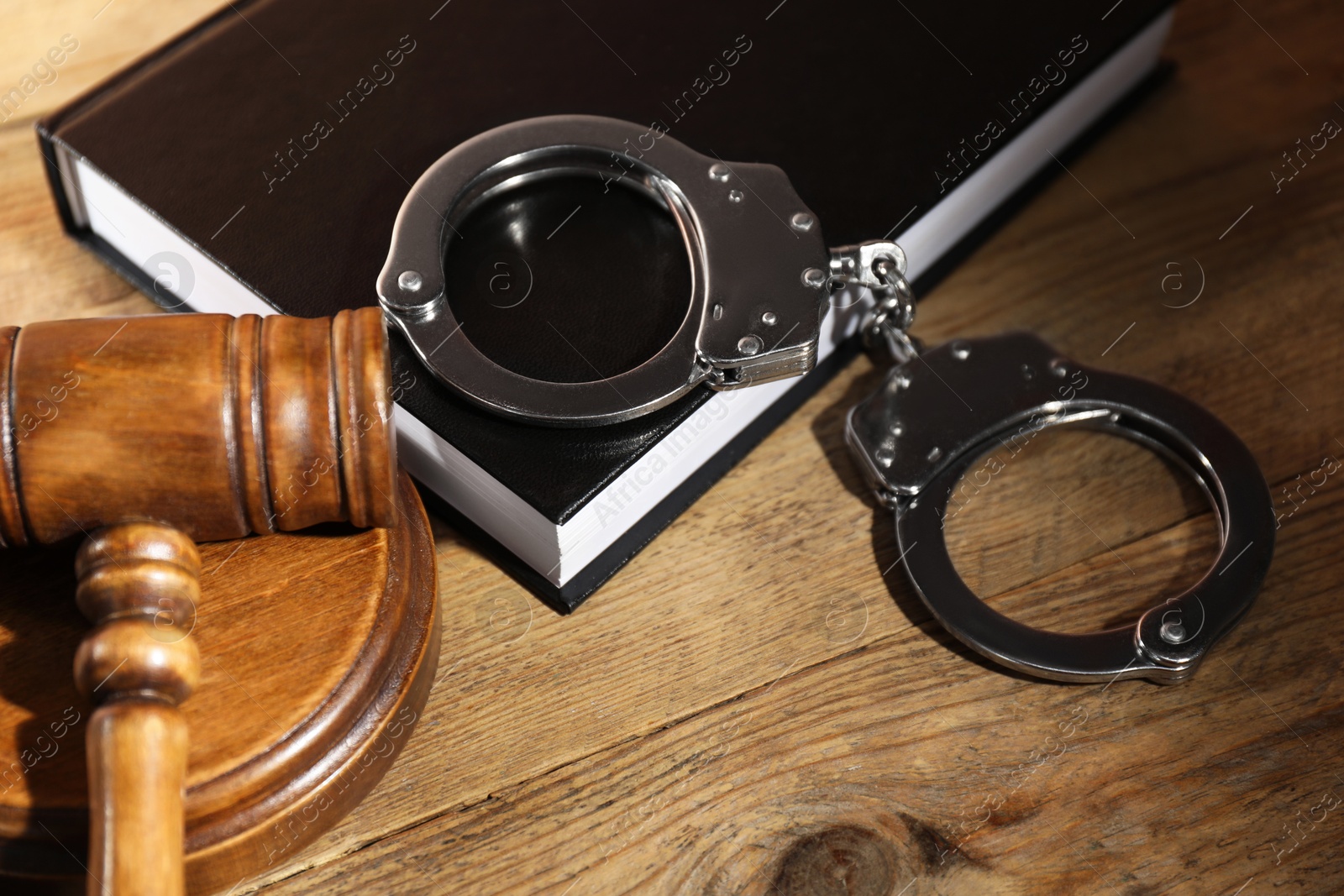 Photo of Book, judge's gavel and handcuffs on wooden table, closeup