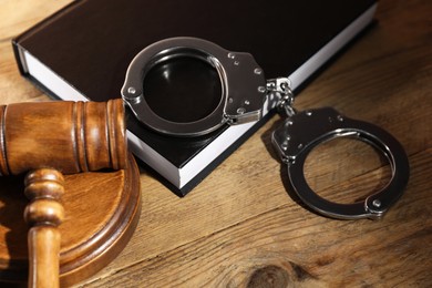 Book, judge's gavel and handcuffs on wooden table, closeup