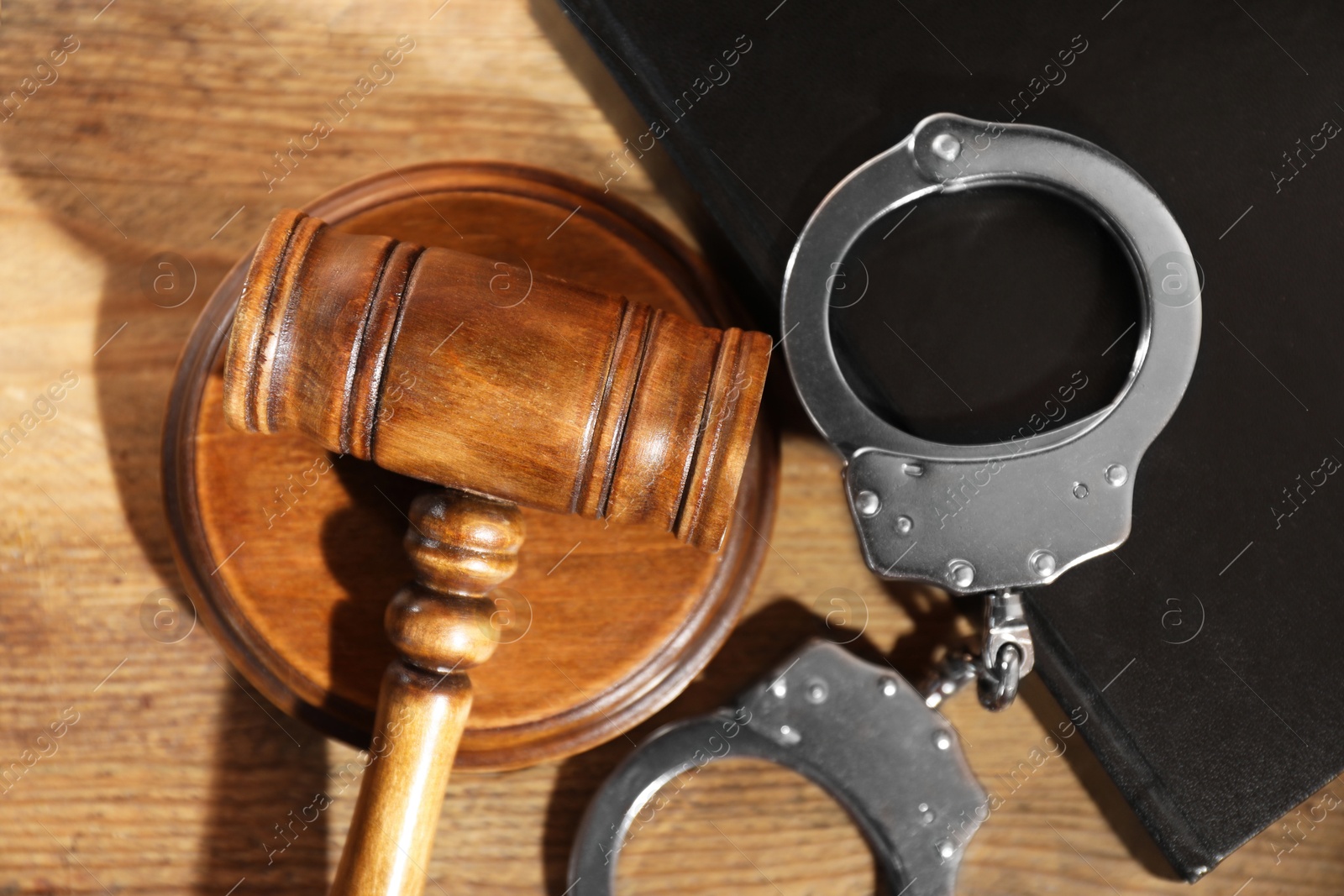 Photo of Book, judge's gavel and handcuffs on wooden table, flat lay