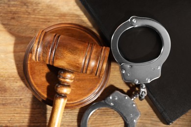 Book, judge's gavel and handcuffs on wooden table, flat lay