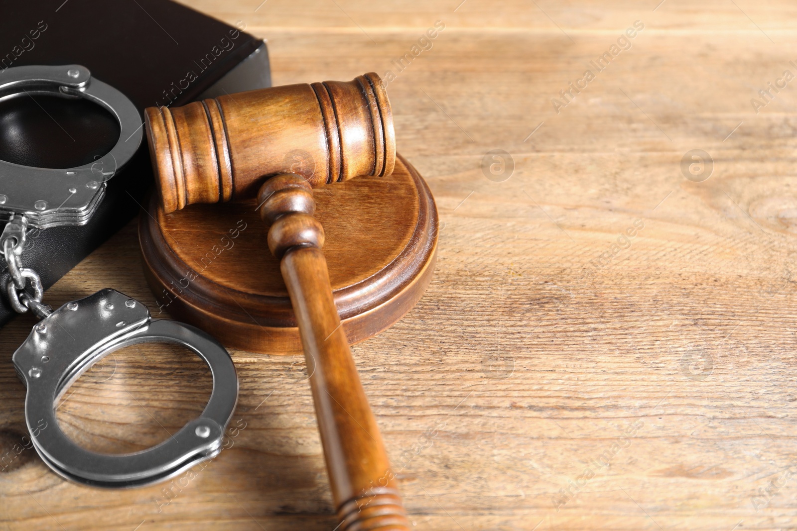 Photo of Book, judge's gavel and handcuffs on wooden table, closeup. Space for text