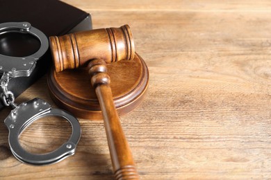 Photo of Book, judge's gavel and handcuffs on wooden table, closeup. Space for text