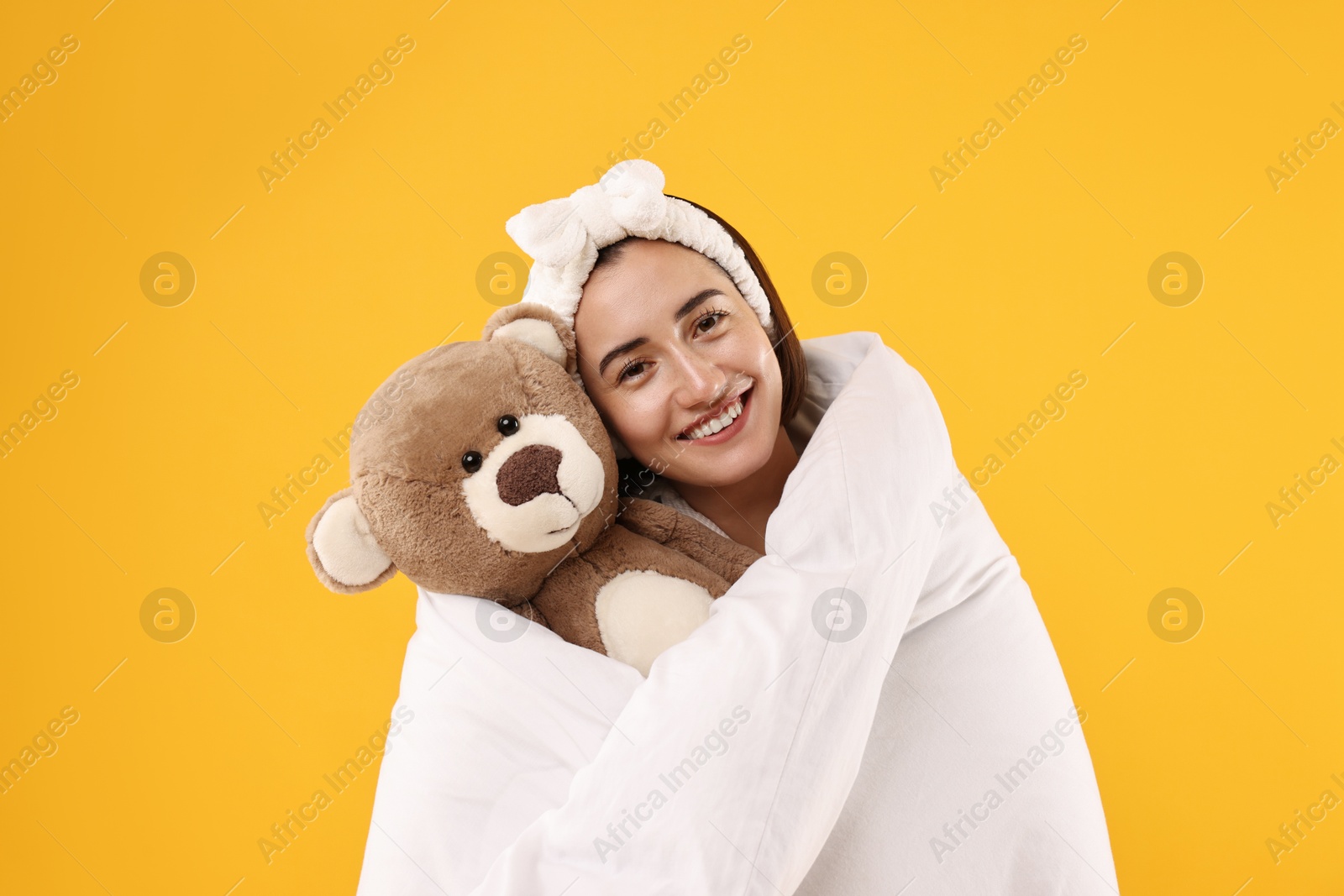 Photo of Happy young woman with teddy bear wrapped in blanket on yellow background