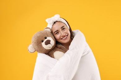 Photo of Happy young woman with teddy bear wrapped in blanket on yellow background