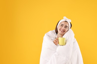 Photo of Happy young woman with cup wrapped in blanket on yellow background. Space for text