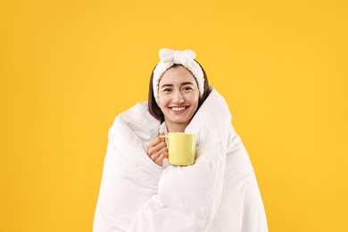 Photo of Happy young woman with cup wrapped in blanket on yellow background