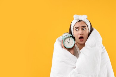 Photo of Overslept young woman with alarm clock wrapped in blanket on yellow background. Space for text