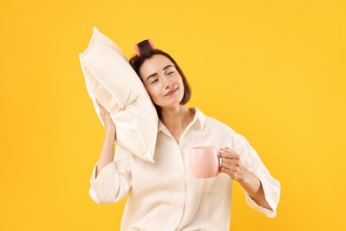 Overslept young woman with pillow and cup on yellow background