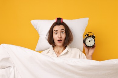 Photo of Overslept young woman with alarm clock, pillow and blanket on yellow background