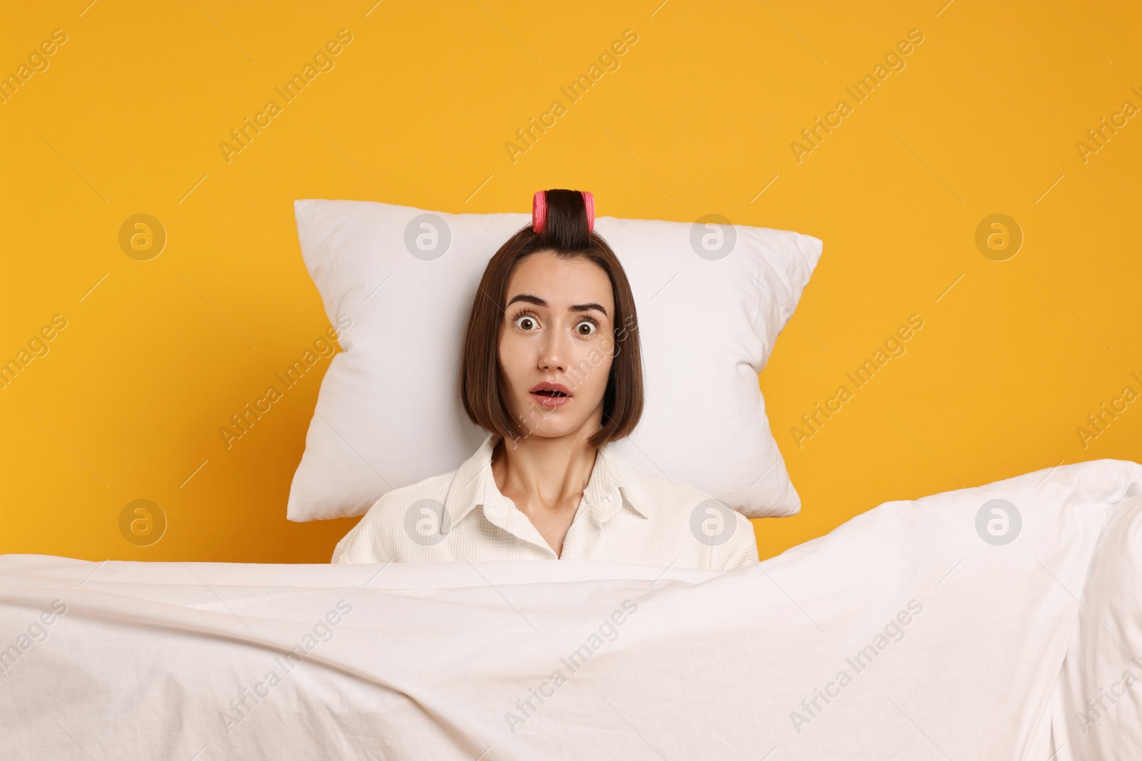 Photo of Overslept young woman with pillow and blanket on yellow background