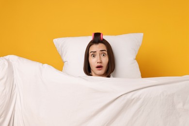 Photo of Overslept young woman with pillow and blanket on yellow background