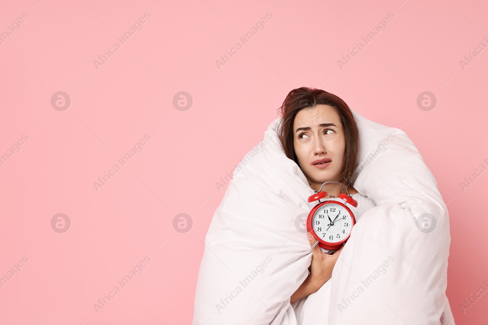 Photo of Overslept young woman with alarm clock wrapped in blanket on pink background. Space for text