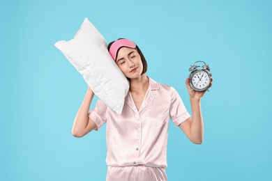 Photo of Overslept young woman with sleep mask, pillow and alarm clock on light blue background