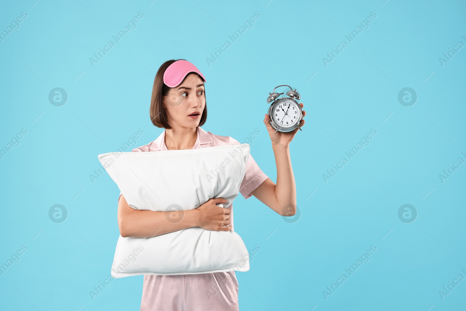 Photo of Overslept young woman with sleep mask, pillow and alarm clock on light blue background. Space for text