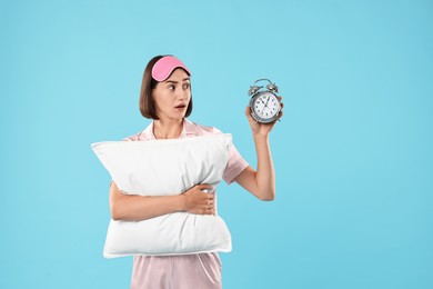 Overslept young woman with sleep mask, pillow and alarm clock on light blue background. Space for text