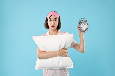 Overslept young woman with sleep mask, pillow and alarm clock on light blue background