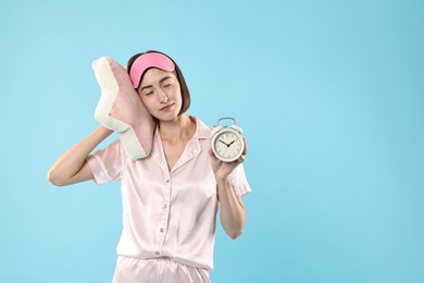 Overslept young woman with sleep mask, pillow and alarm clock on light blue background. Space for text