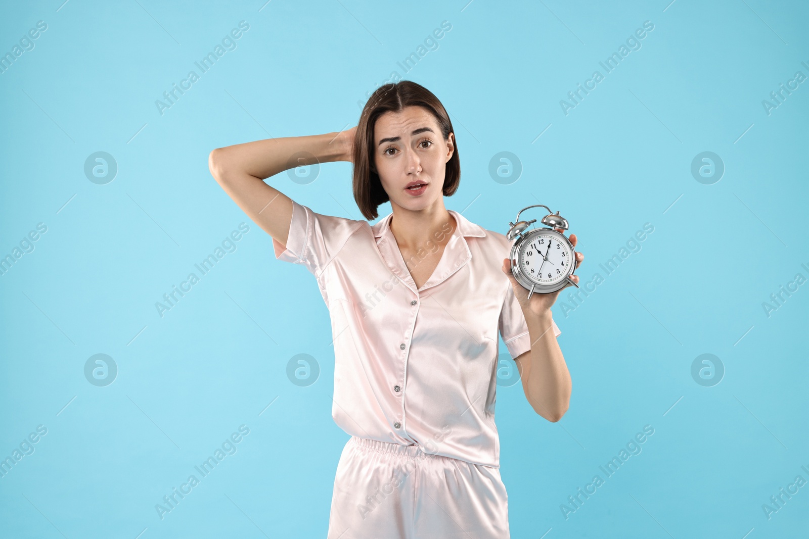 Photo of Overslept young woman with alarm clock on light blue background